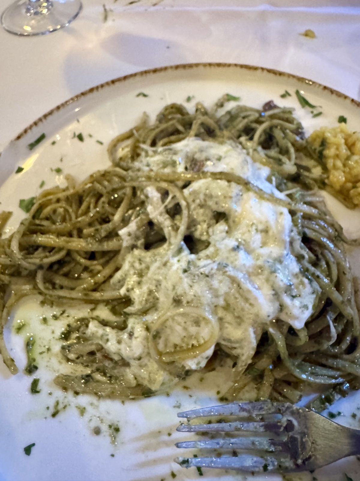 A large plate of spaghetti in a green herb sauce, topped with melted cheese
          and scattered with chopped herbs, a fork resting at the edge of the plate.
