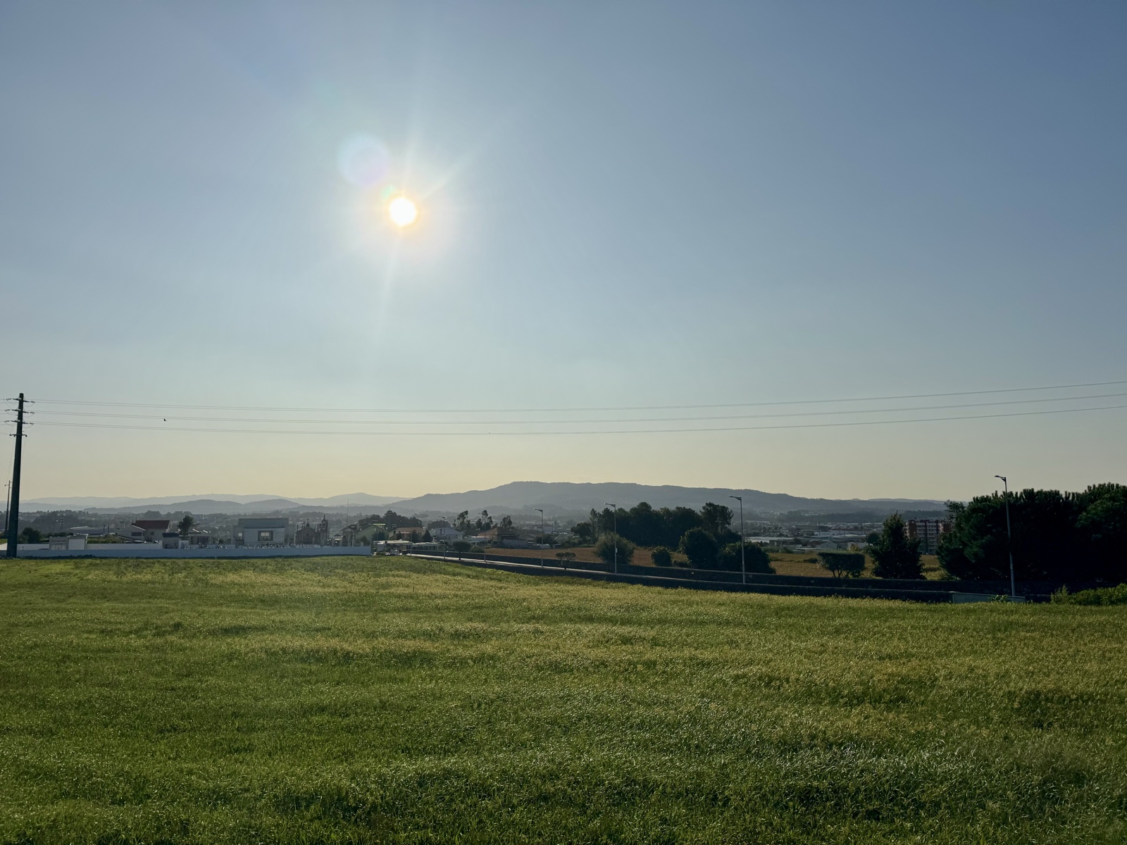 The morning sun over a wide green field, farmland and distant hills beyond.