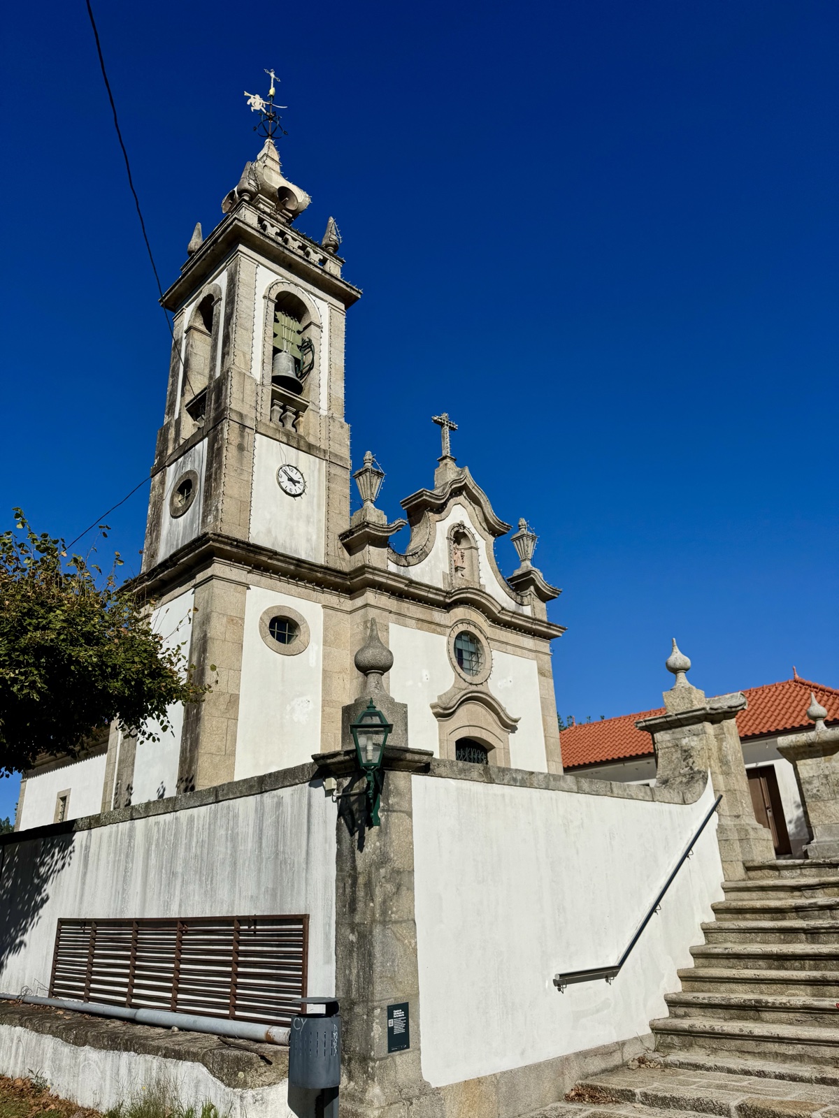A white church with a stone bell tower and a flight of steps, against a deep blue sky.