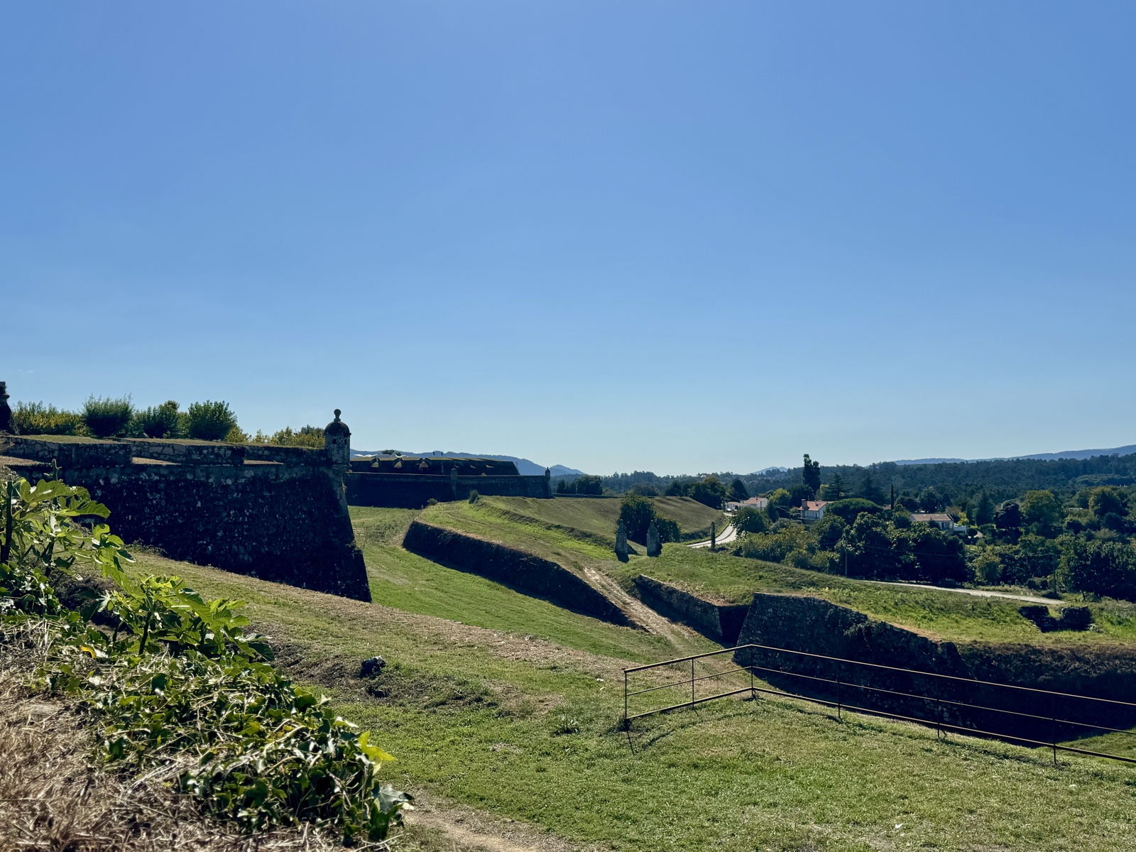 The grassy moats and angled stone ramparts of the Valença fortress, green hills beyond.