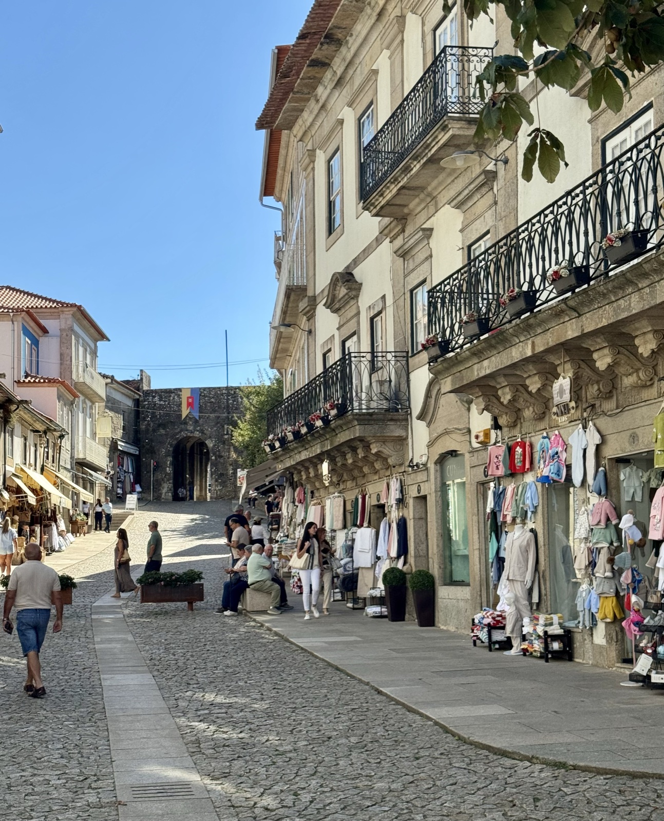 A cobbled street in Valença lined with shops selling linens and towels under wrought-iron balconies.