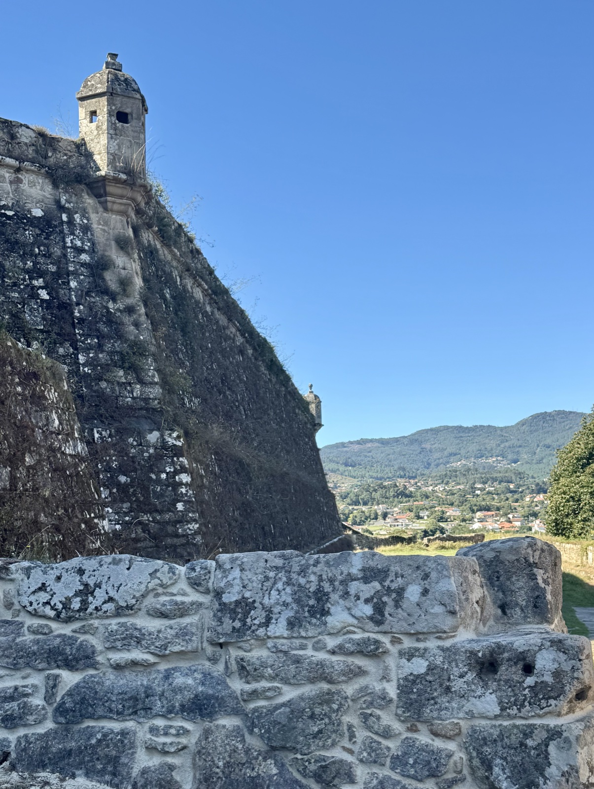 A corner watchtower on the fortress wall, mountains across the valley below.
