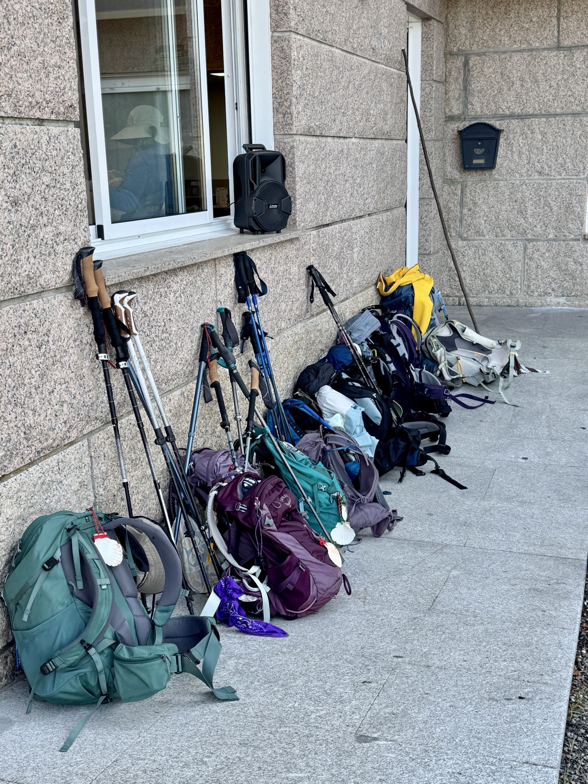 A dozen backpacks and a thicket of trekking poles propped against a stone wall outside a cafe.