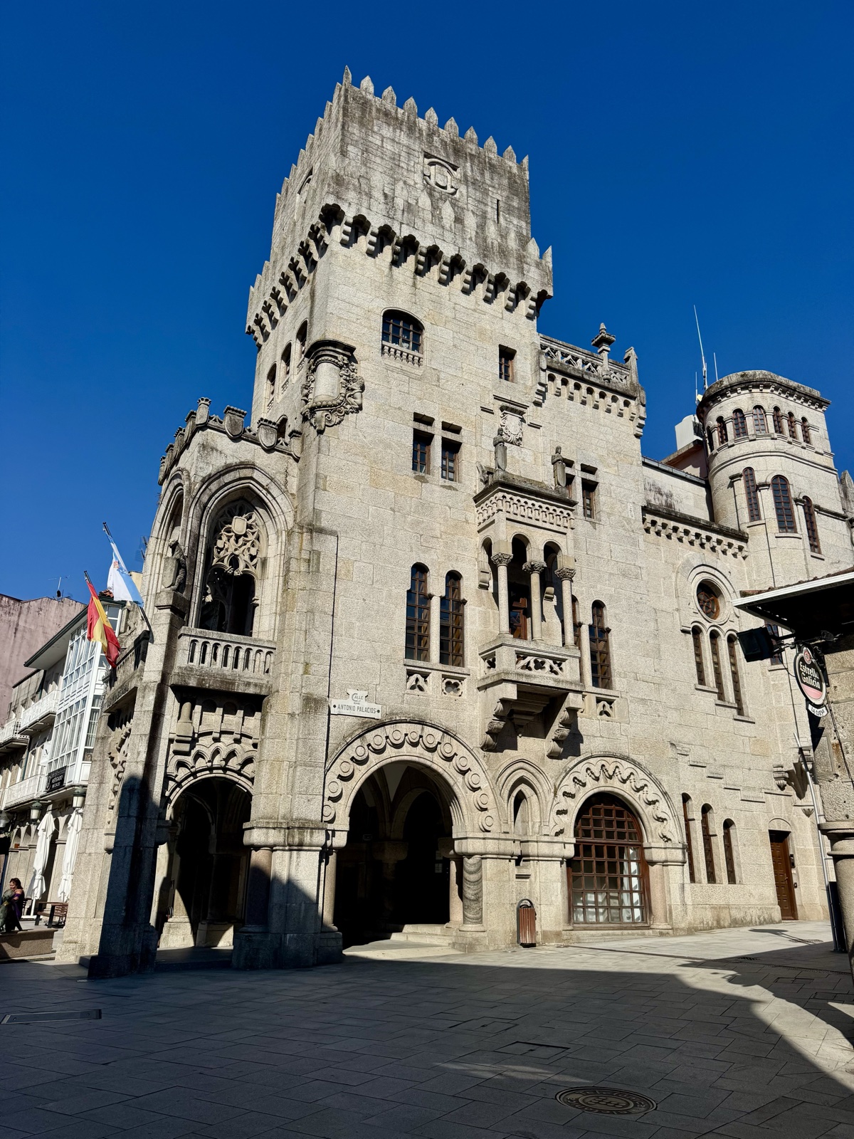 An ornate granite civic building with a battlemented tower and carved arched entrance, seen from the square below.