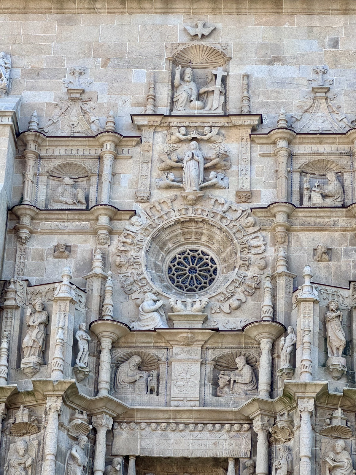 Detail of a carved stone church front, saints in niches around a round rose window.