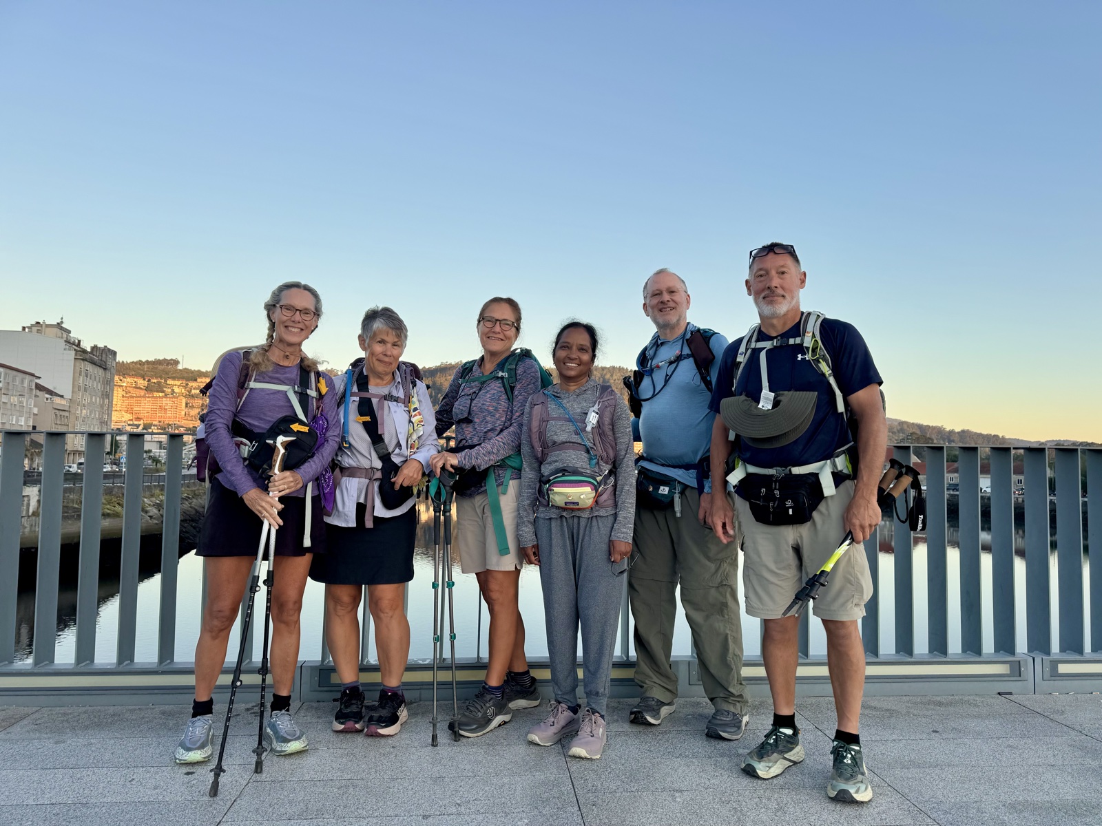 The six pilgrims lined up with their packs and poles on a bridge at sunrise.