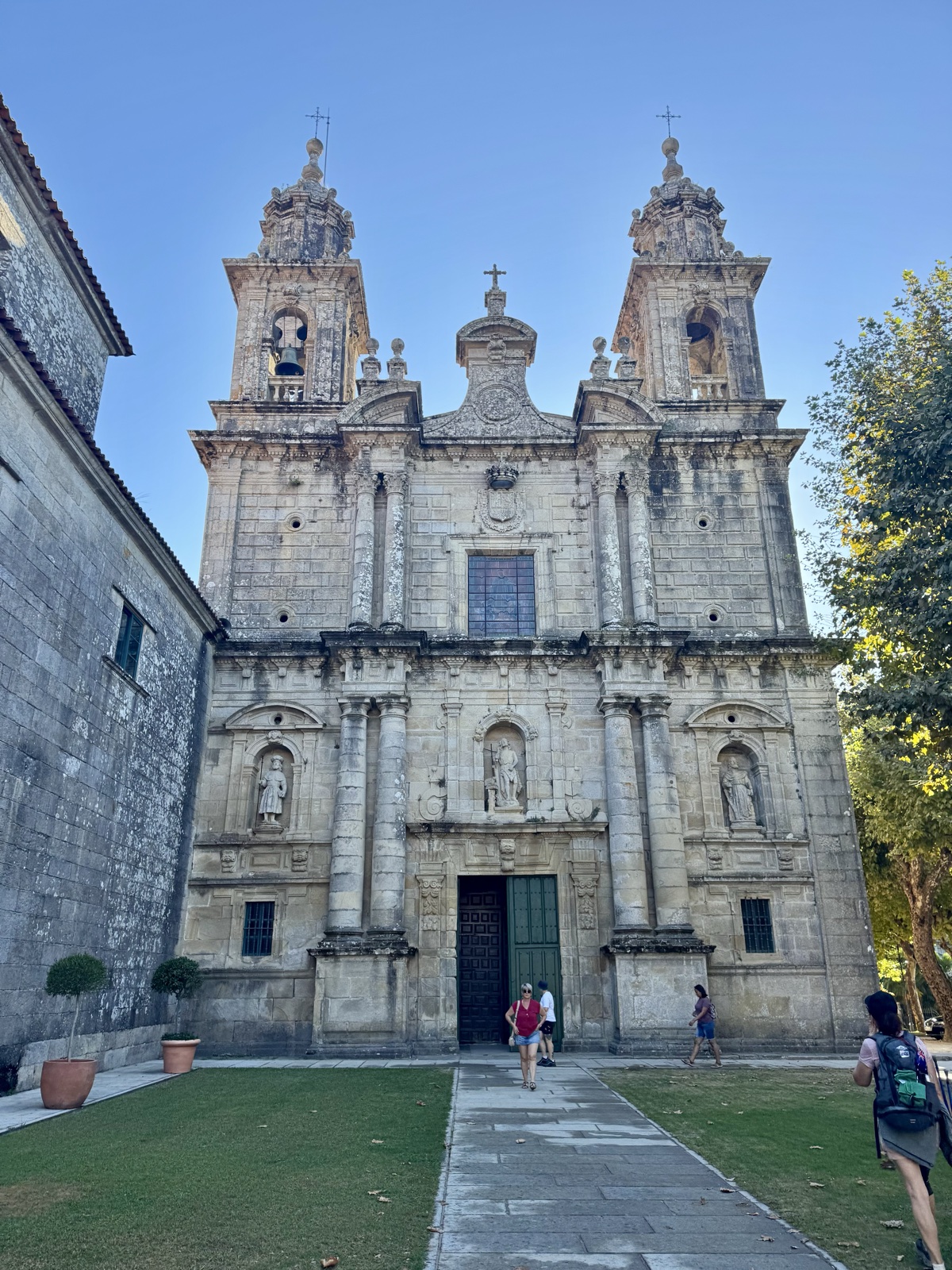 The twin-towered baroque front of a granite monastery, a lawn and path leading to its door.