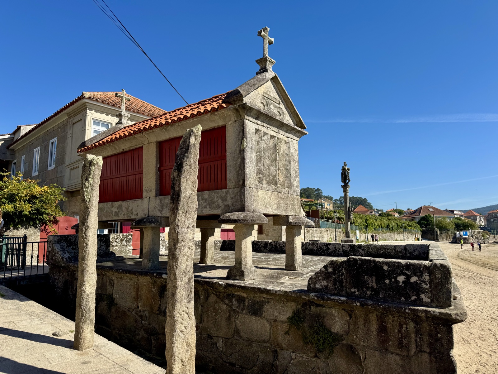 A traditional granite granary raised on stone pillars, topped with a cross, beside the waterfront.