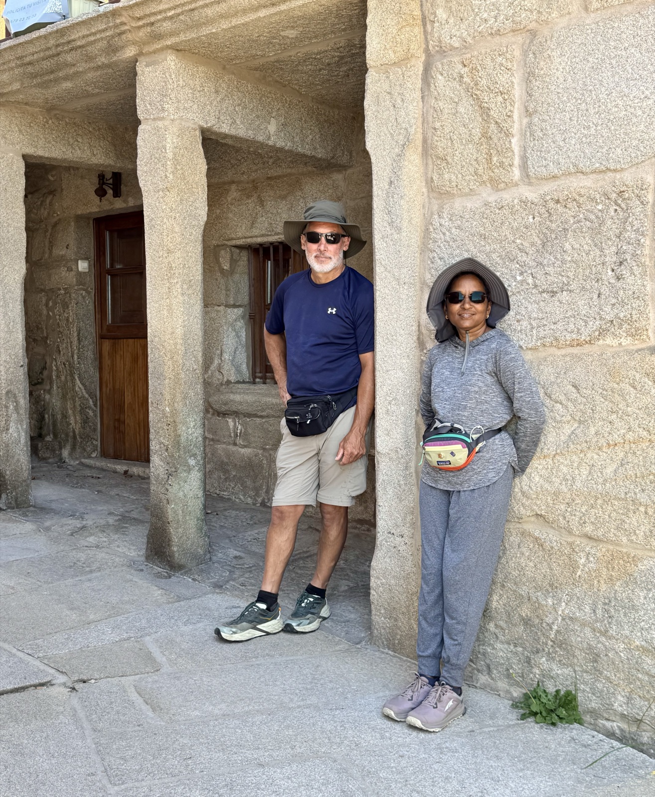 Two pilgrims in hats leaning against the granite pillars of an old arcade.