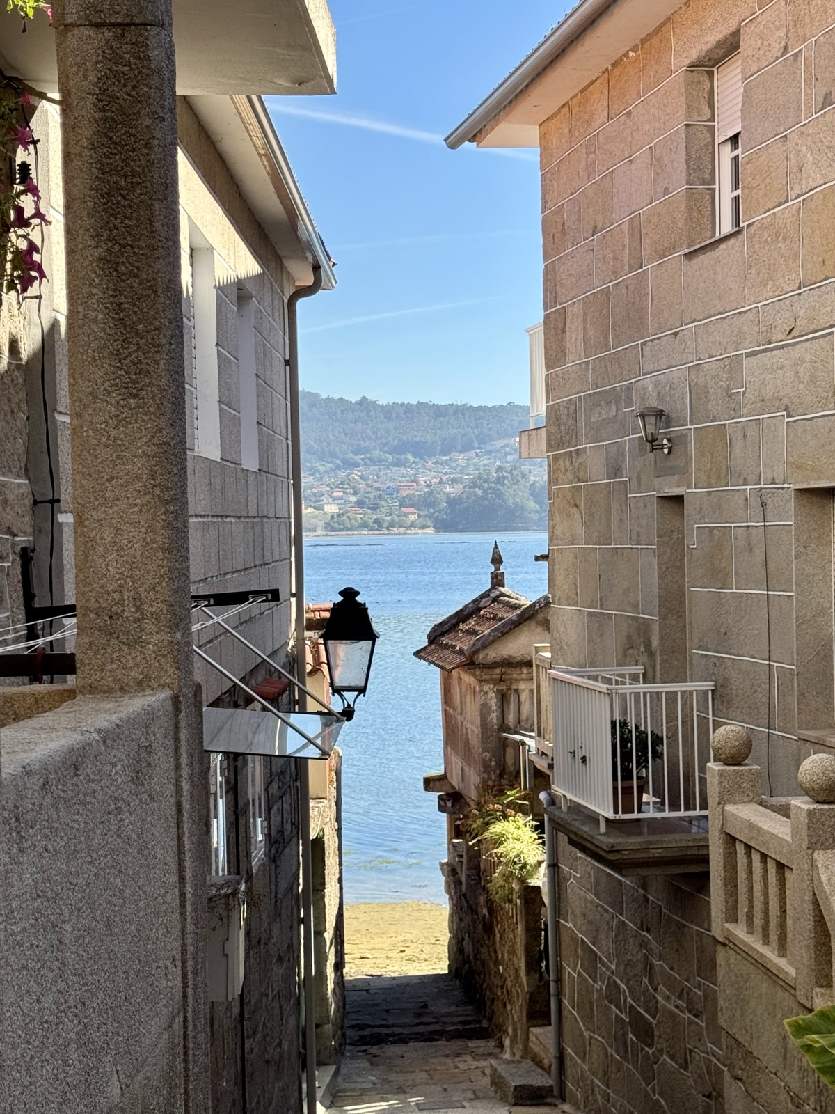 A shaded alley between stone houses opening onto the sea.