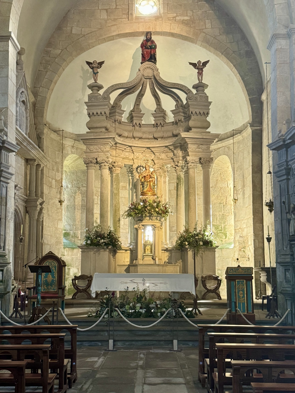 Inside the monastery church, wooden pews leading to an ornate carved stone altar decorated with flowers.