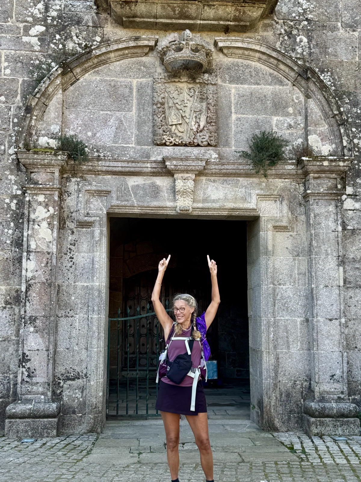 A hiker with a purple pack raising both arms in celebration in front of a carved stone doorway.