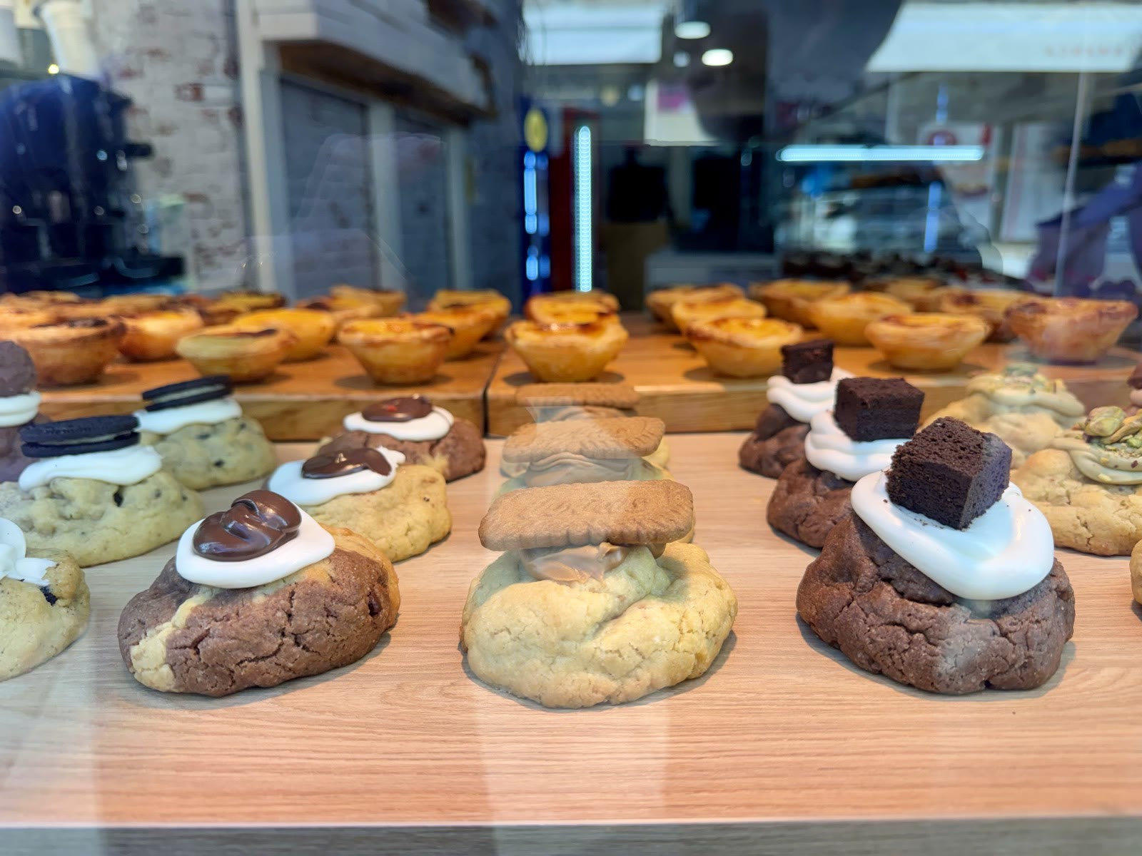 A bakery display case of pastéis de nata and cookies topped with marshmallow cream, chocolate, and biscuit.