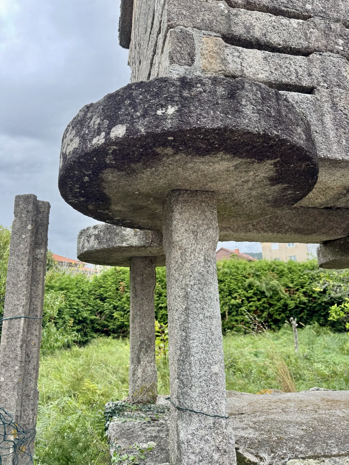 A close view of a corn crib pillar topped with a wide round stone slab.
