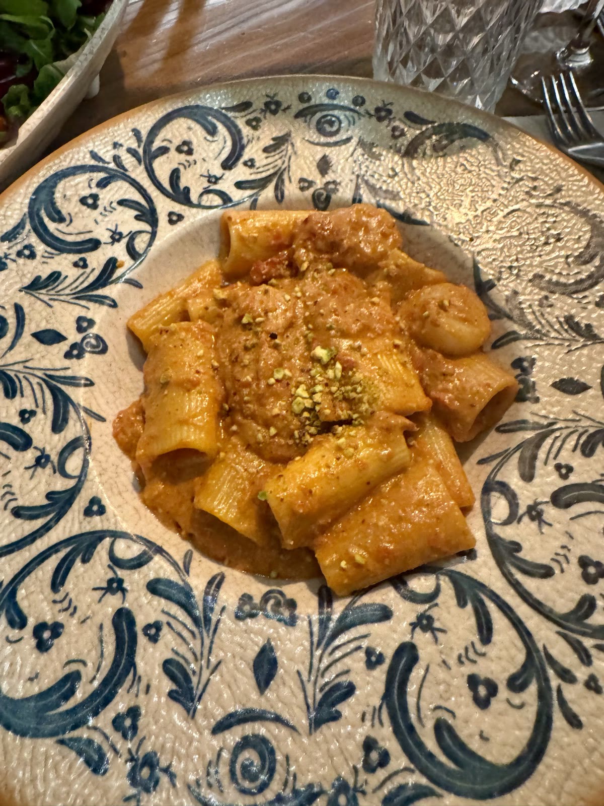 Rigatoni in a creamy tomato sauce with crushed pistachio, on a blue and white patterned plate.