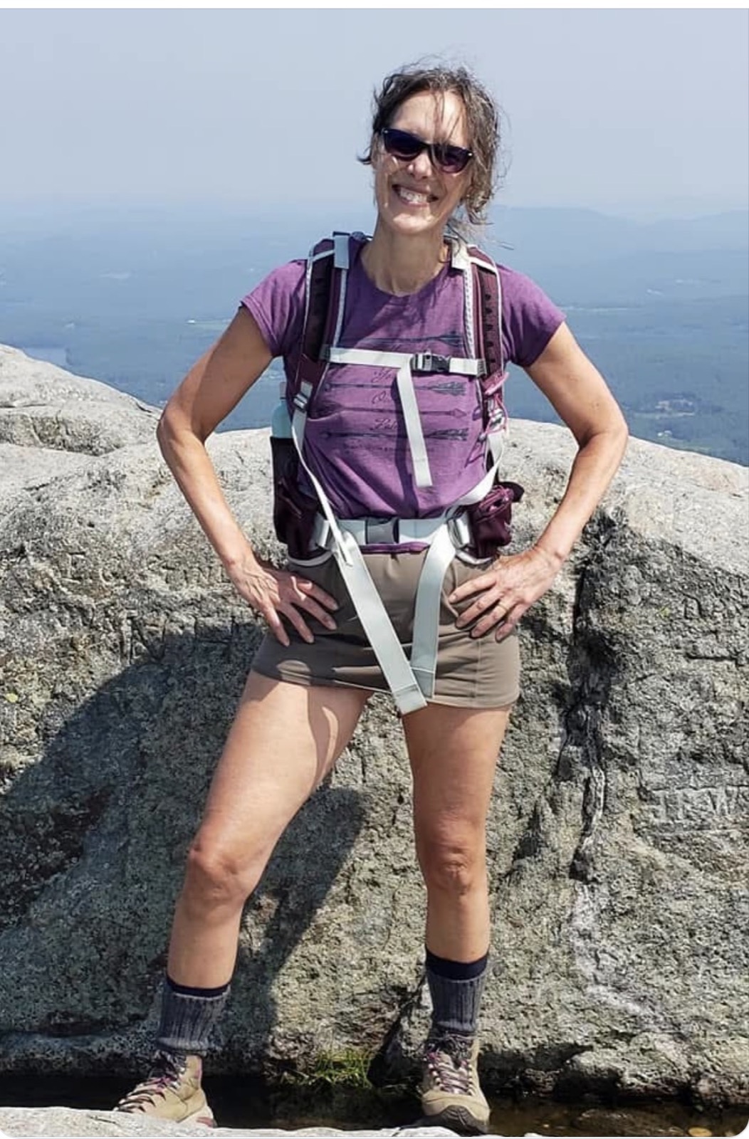 Nancy smiling on a granite outcrop with a mountain view behind her